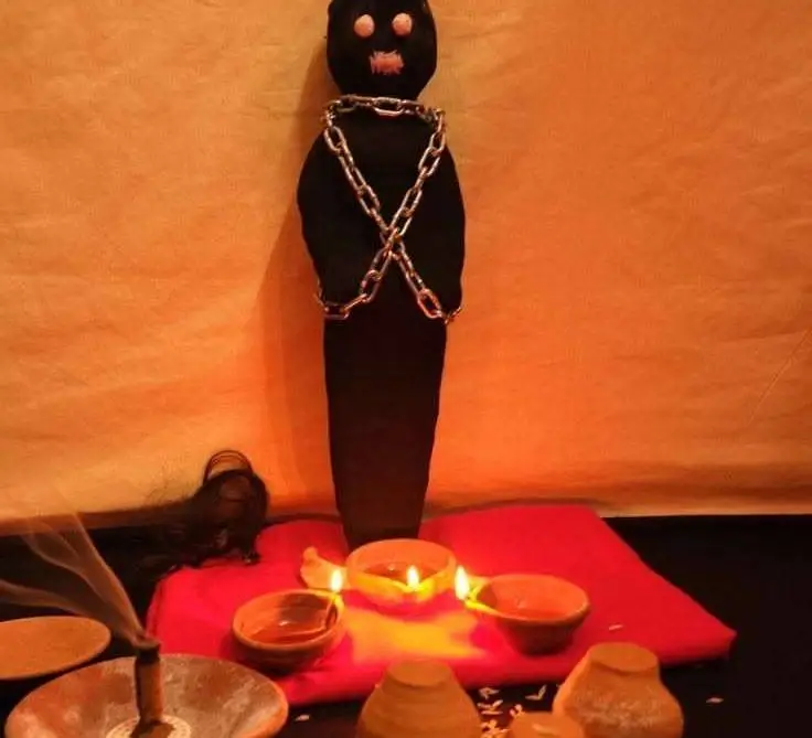 Real Voodoo Love Spell Caster in USA - Chained dark figure on a red cloth altar with small oil lamps